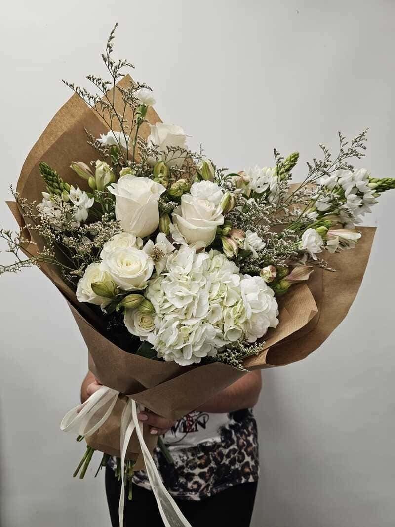 Una persona sostiene un ramo de flores blancas envuelto en papel marrón.