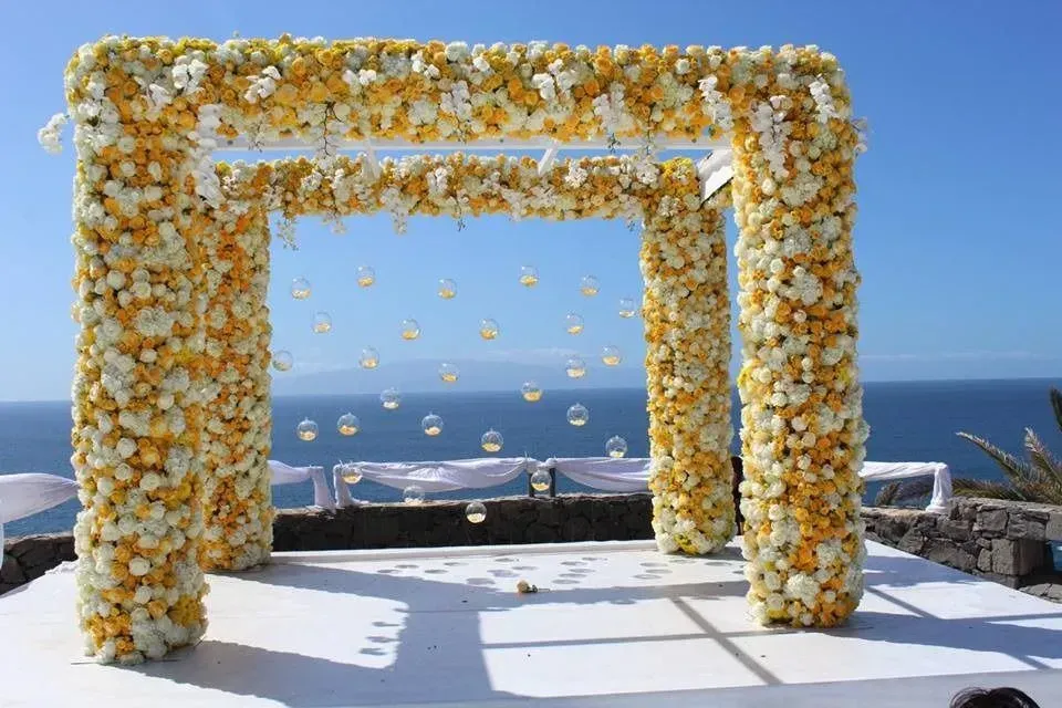 Un arco de boda decorado con flores amarillas y blancas con vistas al océano.