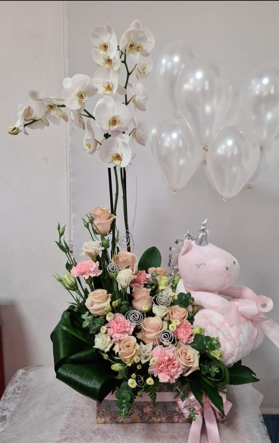 Un osito de peluche rosa está sentado junto a un jarrón de flores.