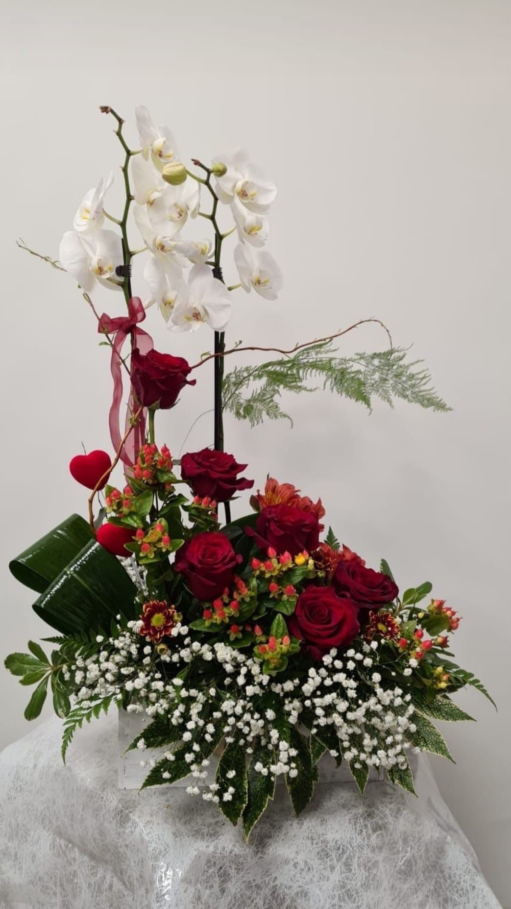 Un jarrón lleno de rosas rojas y orquídeas blancas sobre una mesa.