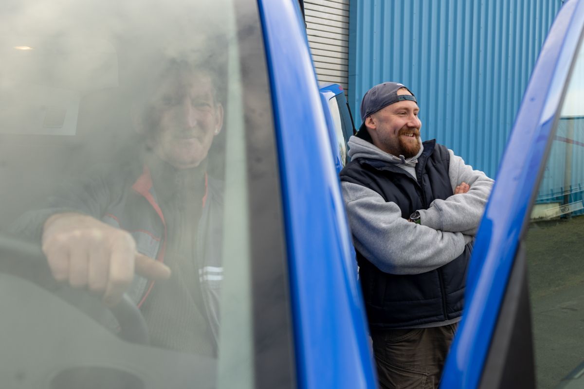 Ein Mann lehnt mit verschränkten Armen an einem blauen Lieferwagen.