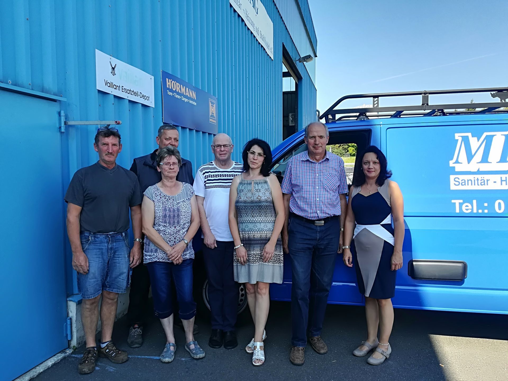 Eine Gruppe von Menschen posiert vor einem blauen Lieferwagen für ein Foto.