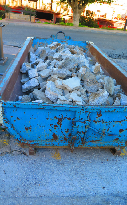 Une benne bleue remplie de gravats blancs et gris repose sur une surface en béton.
