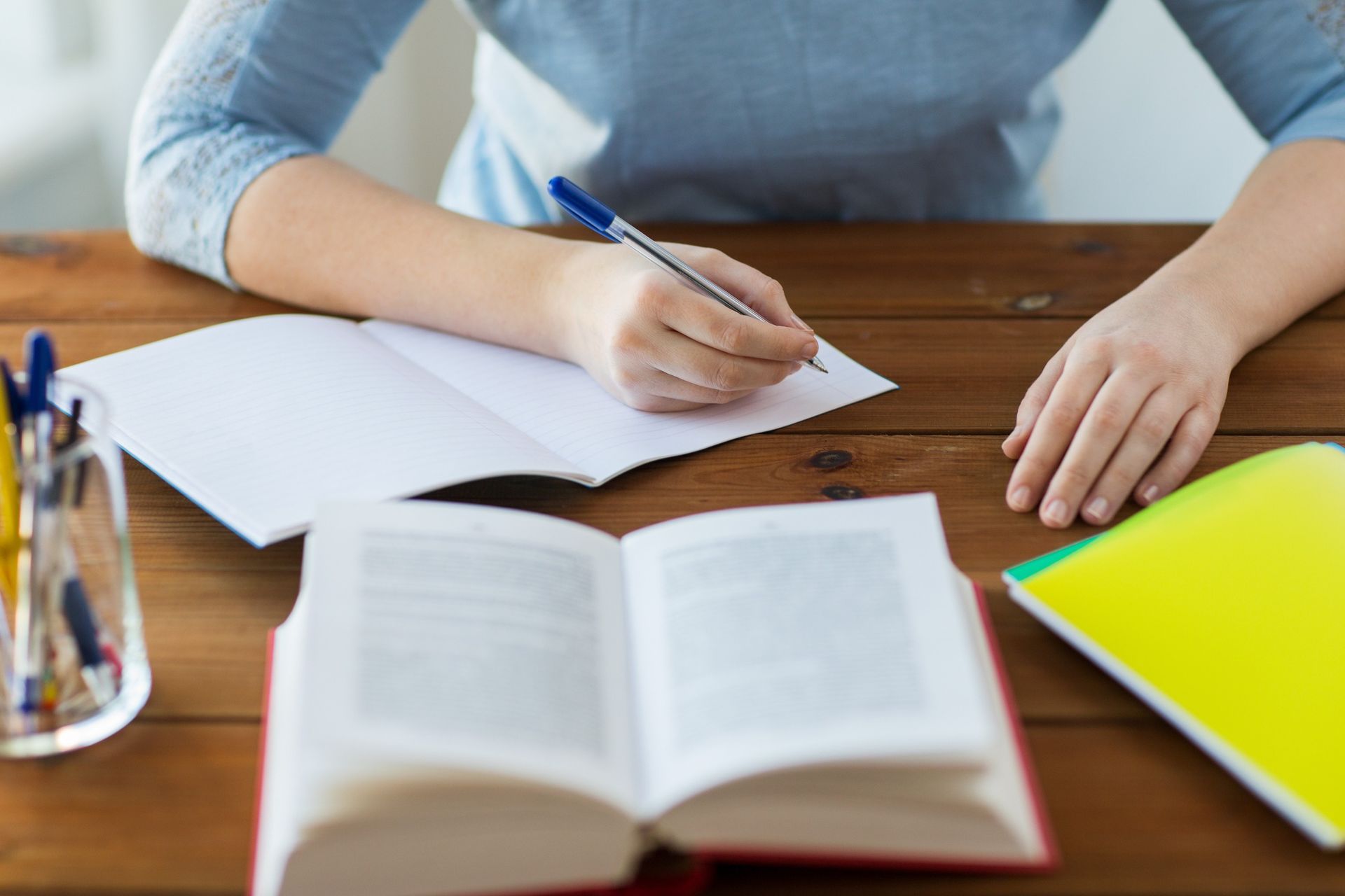Persona escribiendo en un cuaderno en un escritorio de madera con un libro de texto y otro cuaderno.