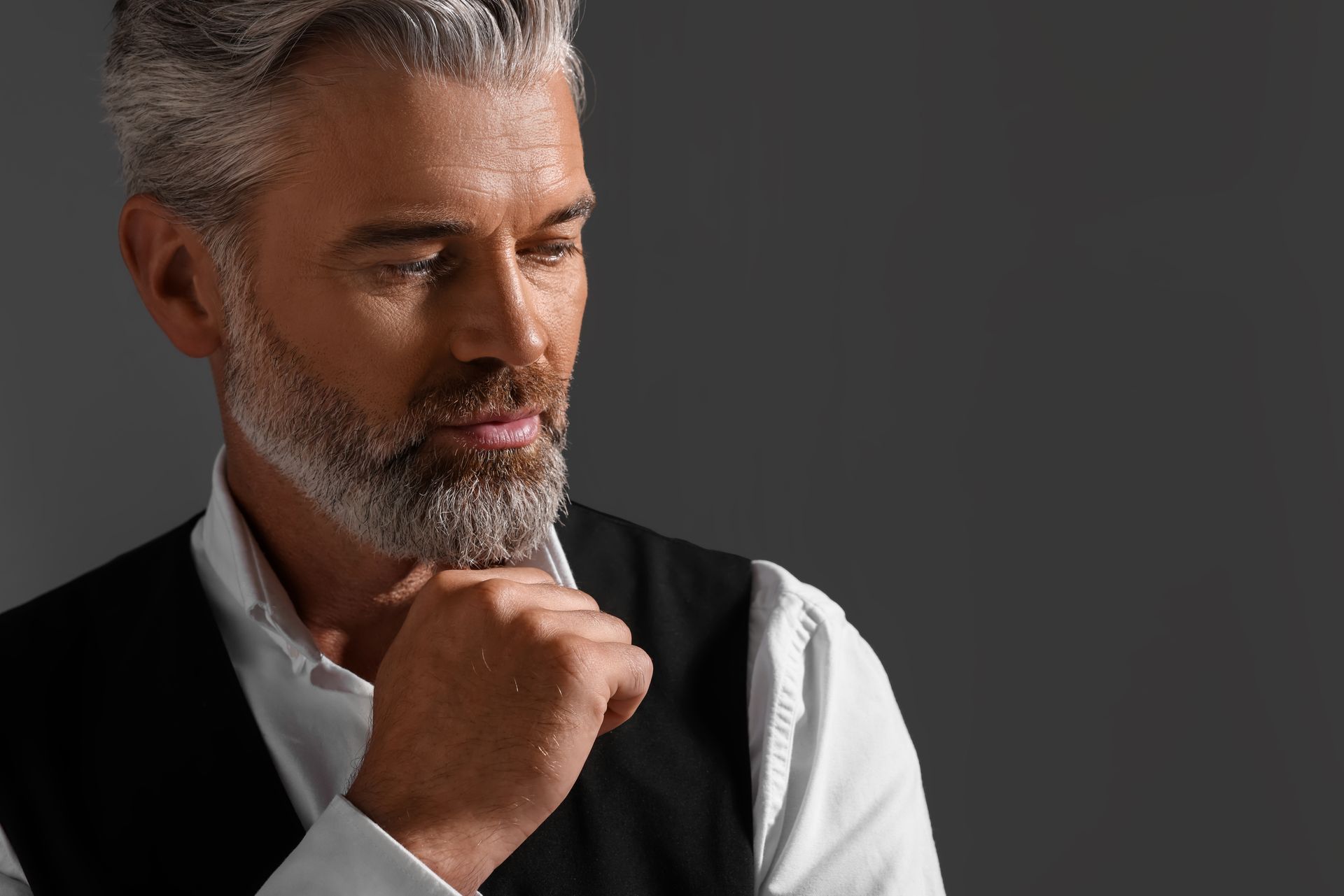 Homme d'âge moyen aux cheveux gris qui a le poing contre sa barbe