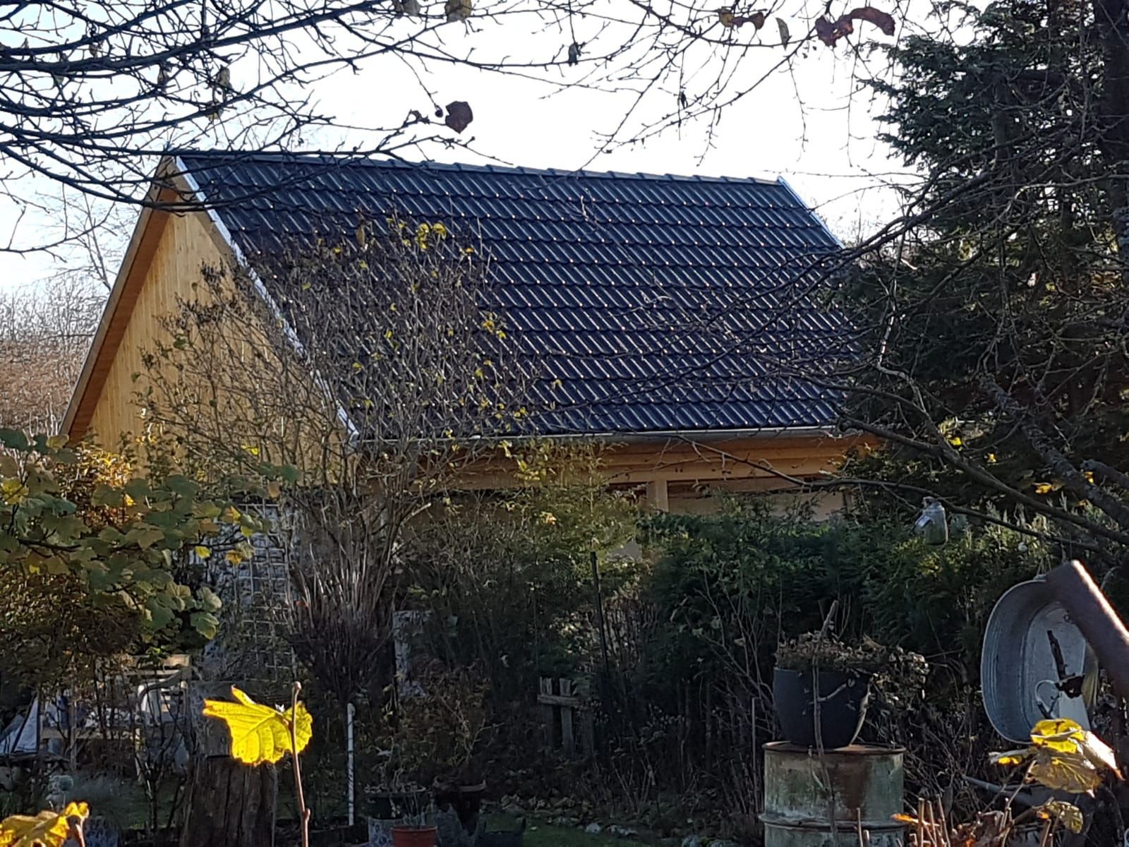 Ein kleines Haus mit schwarzem Dach ist von Bäumen und Büschen umgeben.