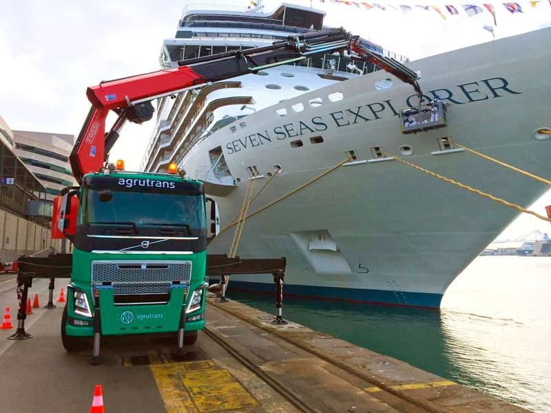 Un camión verde está estacionado frente a un crucero llamado Seven Seas Explorer.