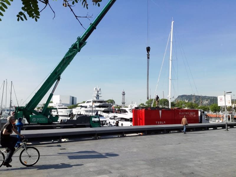Un hombre en bicicleta delante de una gran grúa verde.