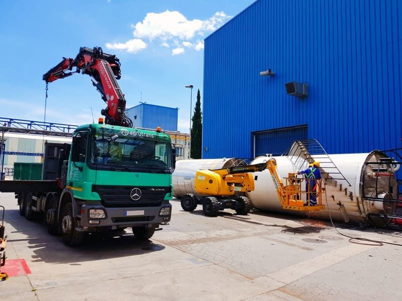 Un camión verde con una grúa en la parte trasera está estacionado frente a un edificio azul.