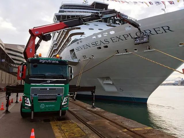 Un camión verde está estacionado frente a un gran crucero llamado Seven Seas Explorer.