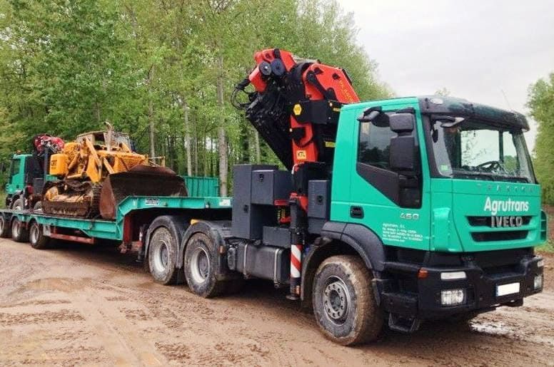 Un camión verde transporta una excavadora en un remolque.