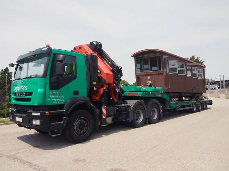 Un camión verde transporta un vagón de tren en un remolque.