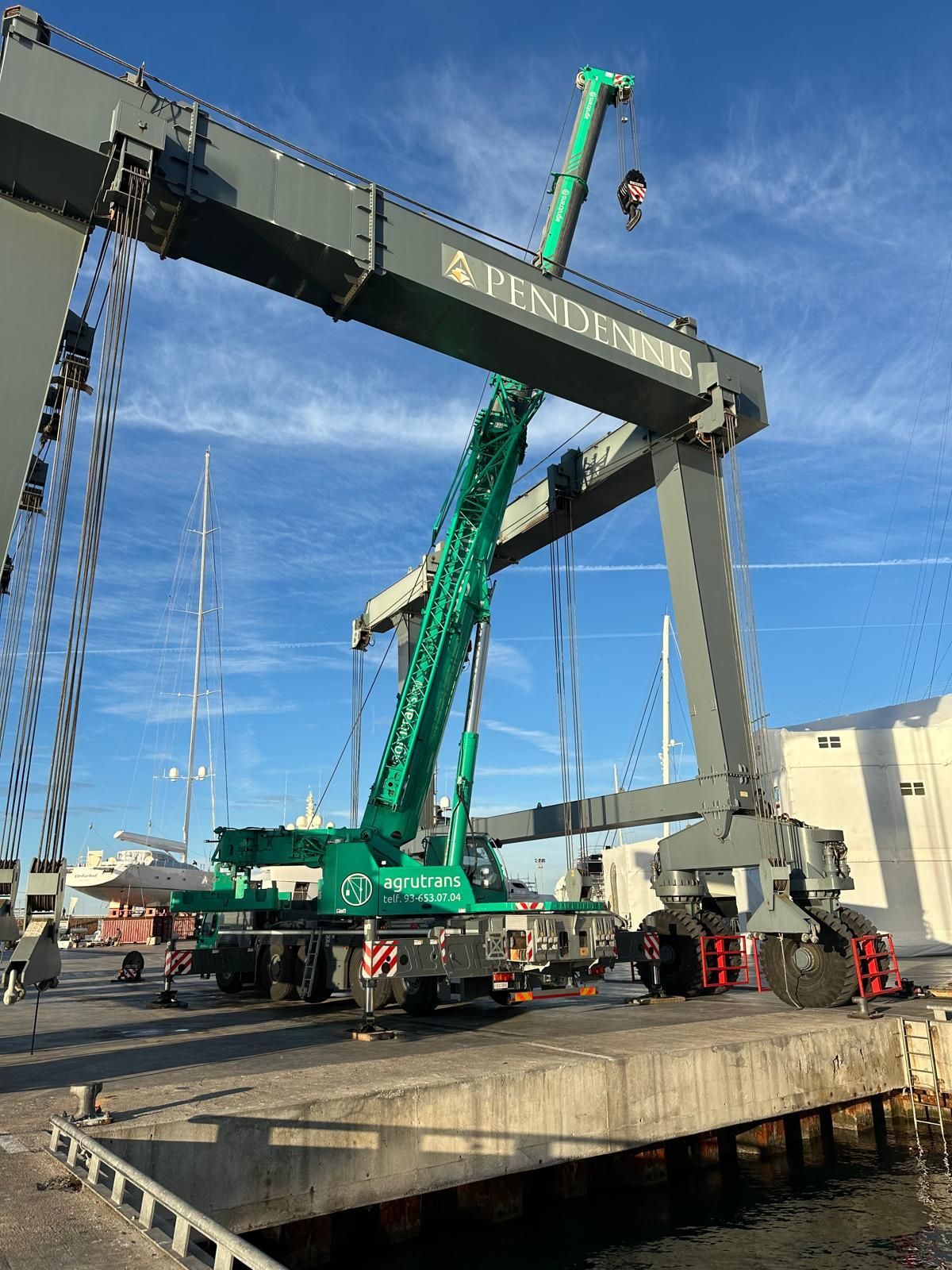 Un hombre en bicicleta delante de una gran grúa verde.