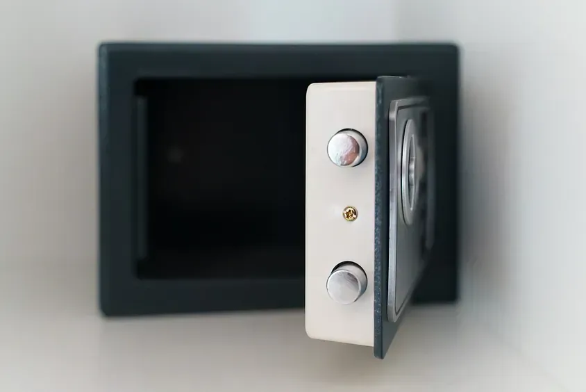 Una caja fuerte abierta reposa sobre una pared blanca.