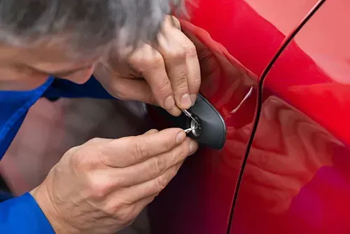 Un hombre está arreglando la cerradura de un coche rojo.