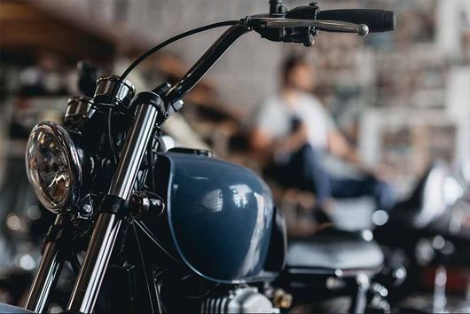 In einer Garage ist ein blaues Motorrad geparkt. Im Hintergrund ist ein Mann zu sehen.