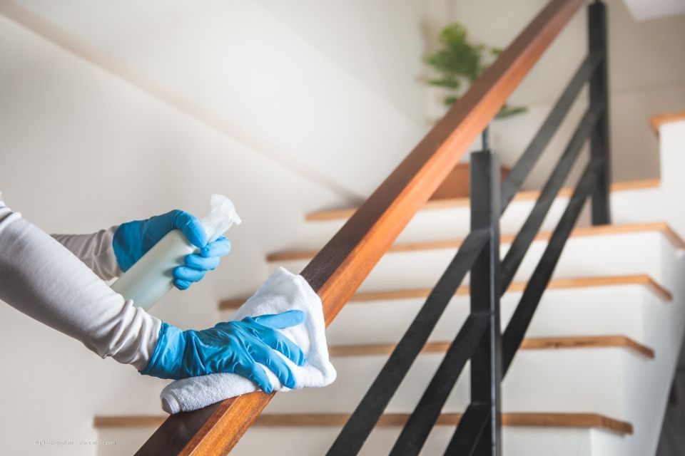 Blitz Blank – Reinigungsfachkraft mit Schutzhandschuhen wischt den hölzernen Handlauf einer Treppe