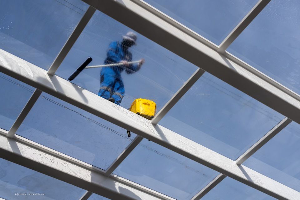 Blitz Blank – Sicht von unten auf ein Glasdach, auf dem eine Reinigungsfachkraft steht, um die Scheiben zu reinigen