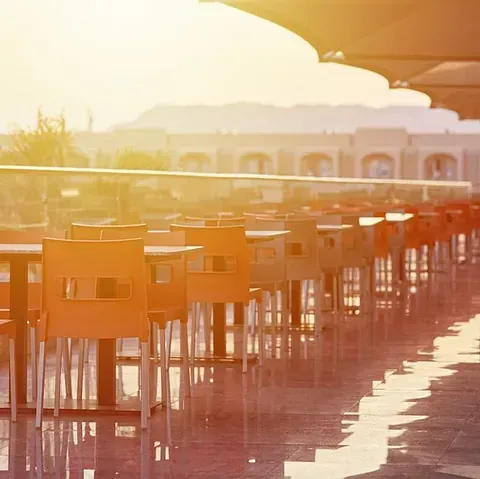 Una fila de mesas y sillas en un restaurante con el sol brillando a través de las ventanas.