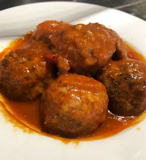 Un plato blanco cubierto con albóndigas y salsa sobre una mesa.