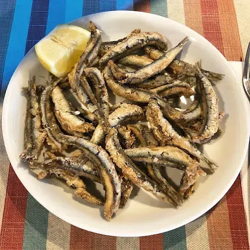 Un plato de sardinas fritas con una rodaja de limón sobre una mesa.