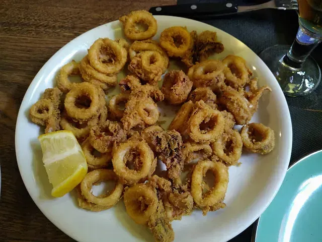 Un plato de calamares fritos con una rodaja de limón sobre una mesa.