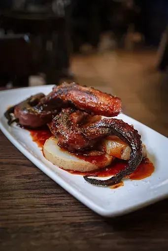 Un plato blanco cubierto con carne y salsa sobre una mesa de madera.