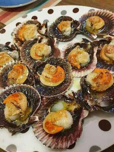 Un plato blanco cubierto con vieiras cocidas sobre una mesa.