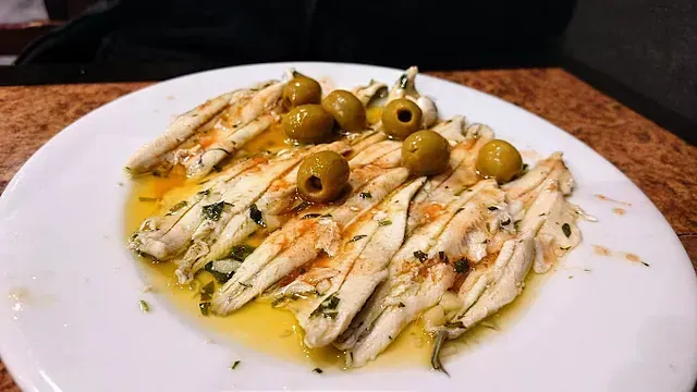 Un plato blanco cubierto con pescado y aceitunas sobre una mesa.