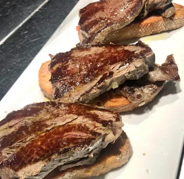 Un plato blanco cubierto con rebanadas de carne y pan.