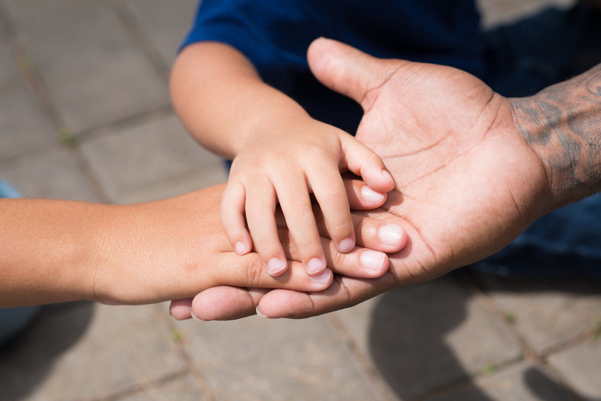 La pequeña mano de un niño descansa en la mano abierta de un adulto, sostenida por otro adulto.