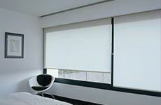 Un dormitorio con una cama, una silla y una ventana con persianas blancas.