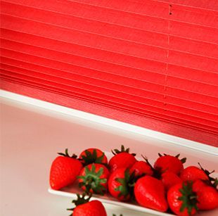 Un plato de fresas se encuentra frente a una persiana roja.