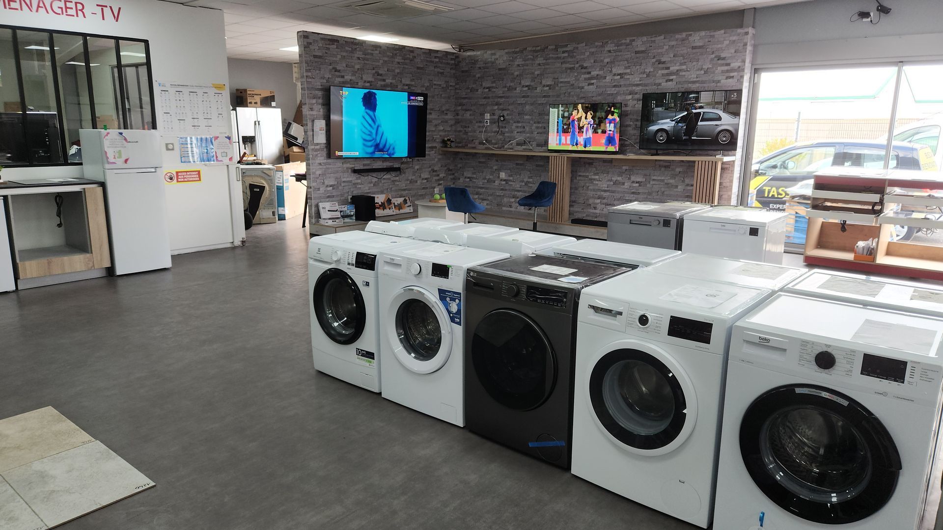 Machines à laver et téléviseurs exposés dans un magasin d'électroménager ; différents modèles et écrans présentés.
