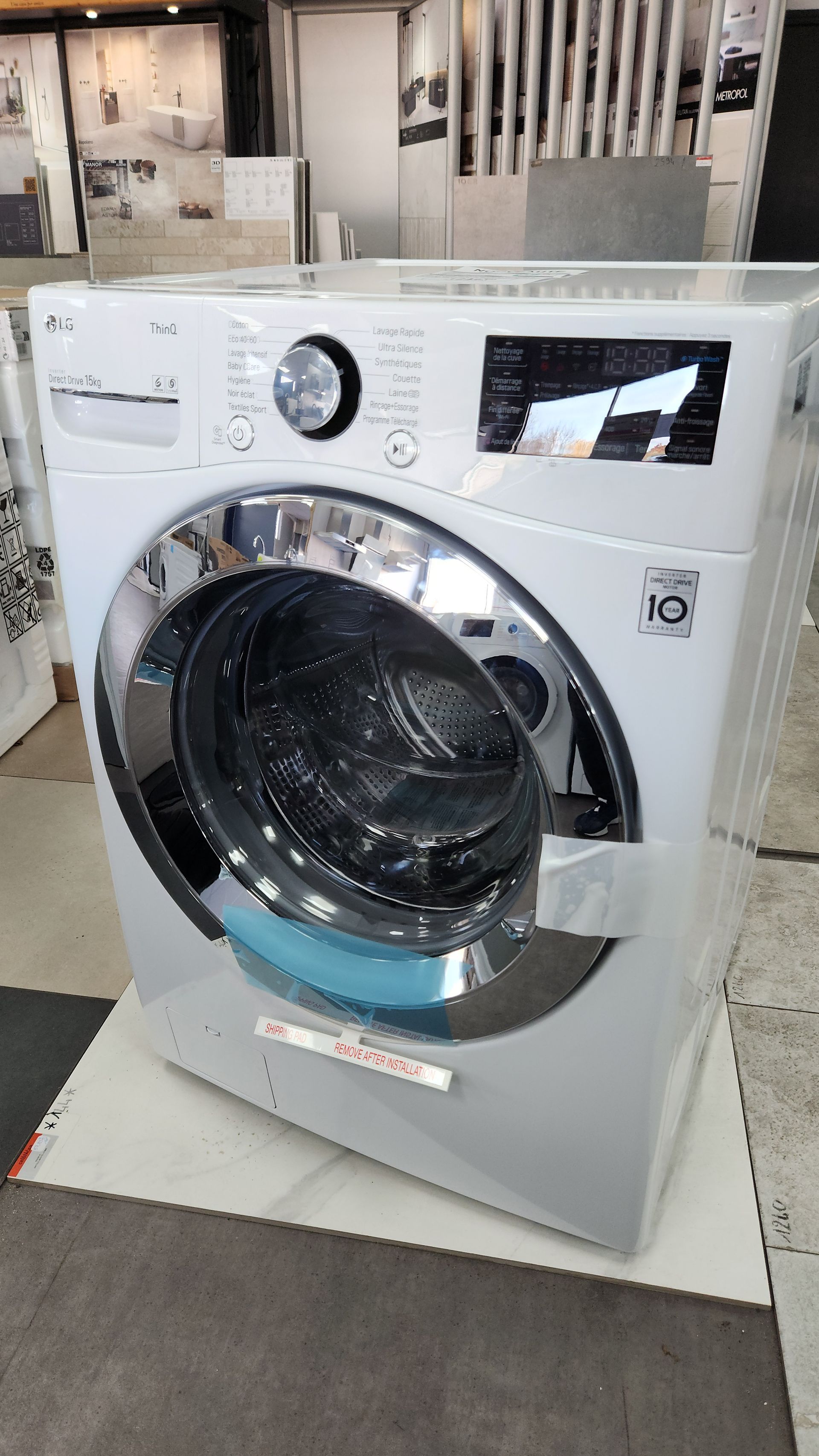 Une machine à laver à chargement frontal LG blanche avec un cadre de porte chromé, à l'intérieur.