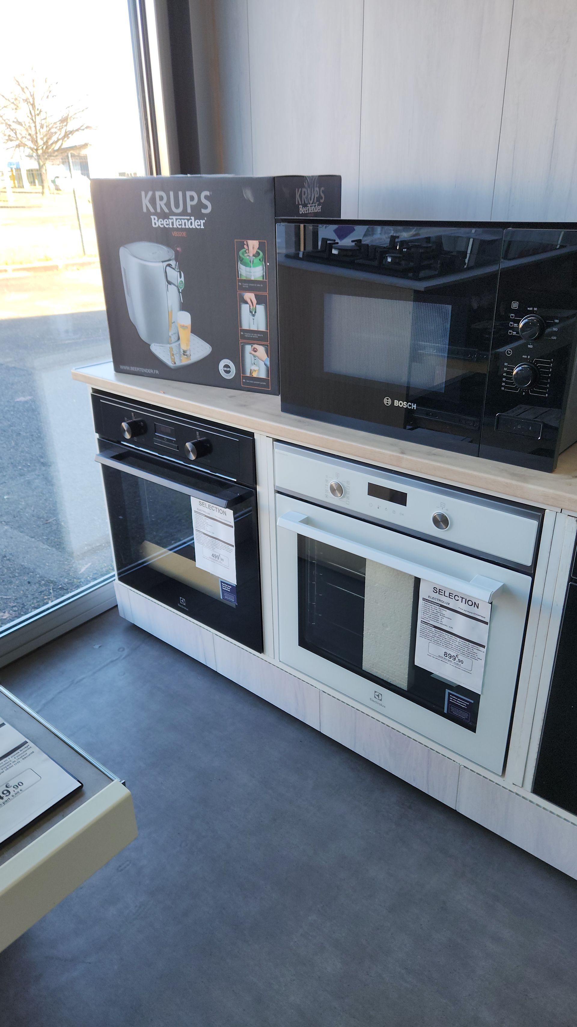 Présentation d'appareils de cuisine : fours, micro-ondes et cafetière sur un comptoir dans un magasin.