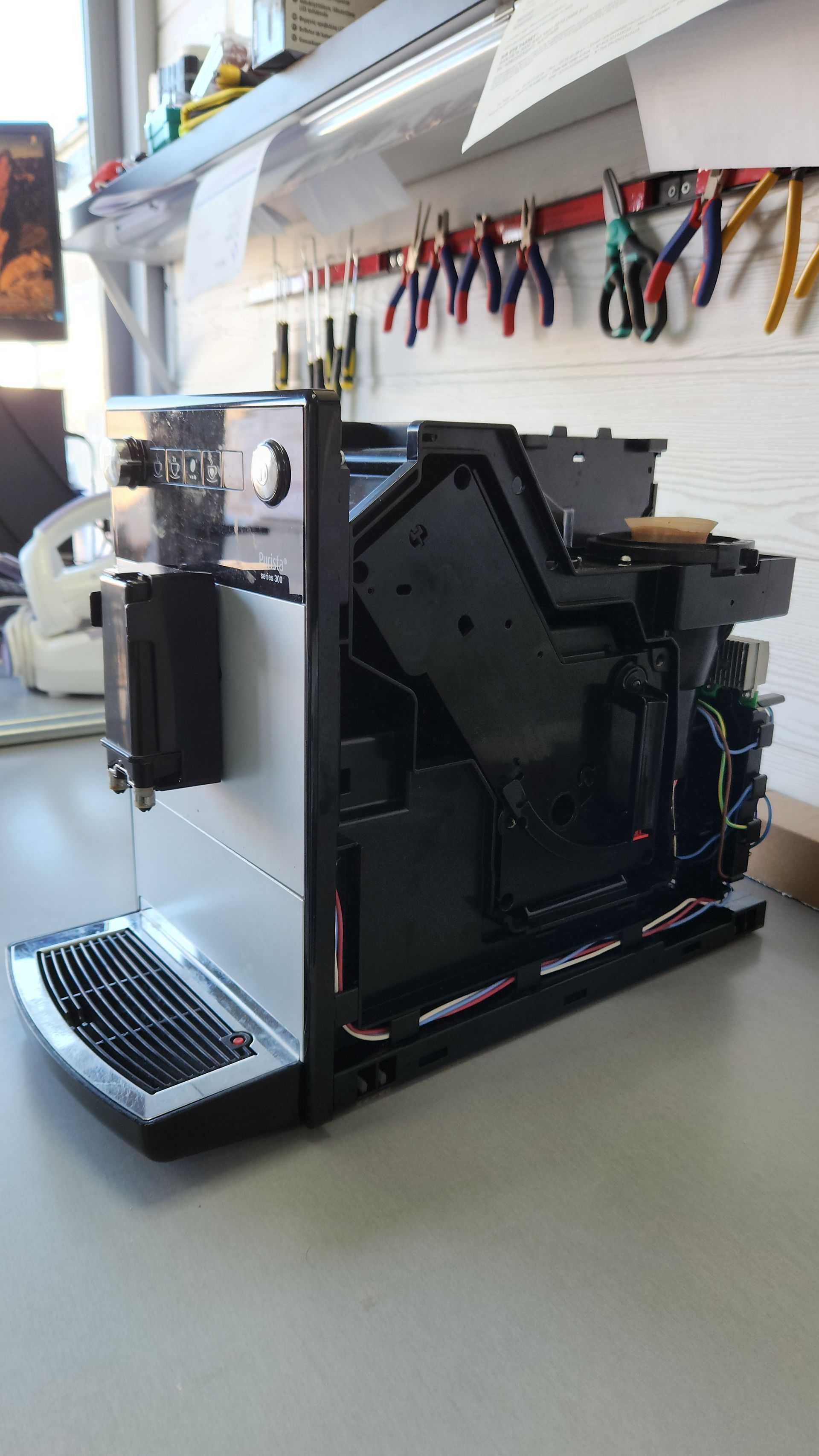 Machine à café partiellement démontée sur un établi ; boîtier noir et argent, composants intérieurs visibles.