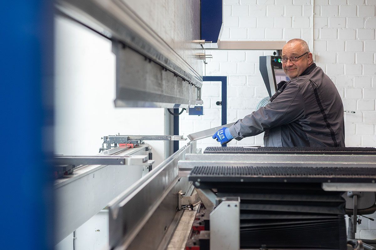 Ein lächelnder Mann bedient in einer Werkstatt eine Metallbiegemaschine.