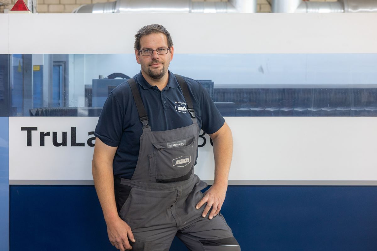 Mann in grauem Overall steht neben einer TruLaser-Maschine.