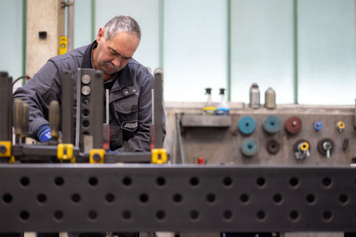 Ein Mann arbeitet an einer Metallbearbeitungsstation und beugt sich über sein Werkstück. Fabrikszene mit Werkzeugen an der Wand.