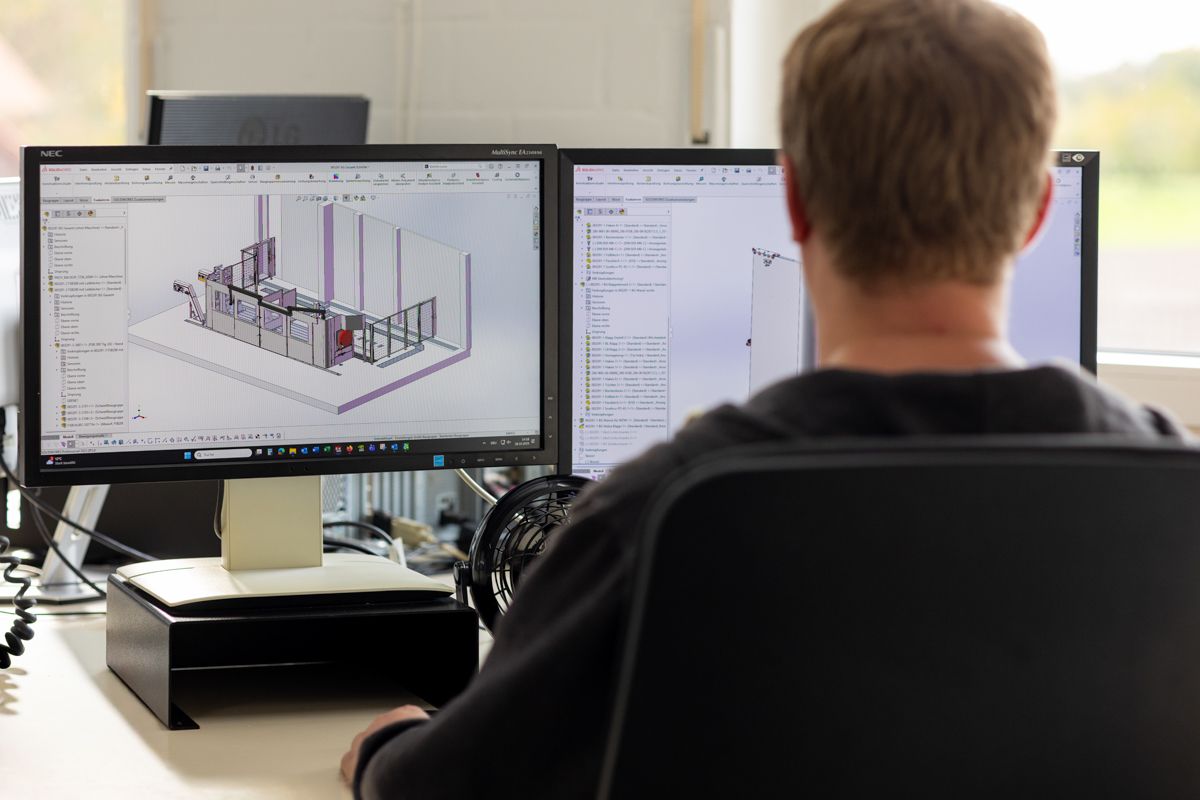Eine Person arbeitet an einem Computer mit zwei Monitoren und zeigt eine 3D-Konstruktion eines Bauwerks an.