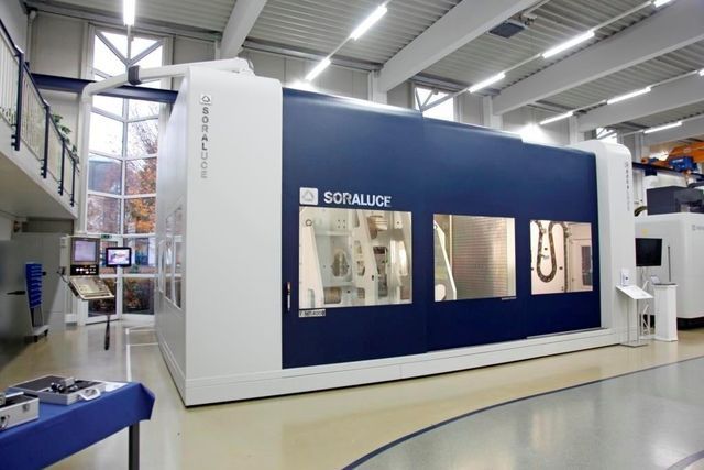 Große, weiß-blaue Industriemaschine in einer Fabrikhalle. Die Maschine hat Fenster und das Logo „SORALUCE“.