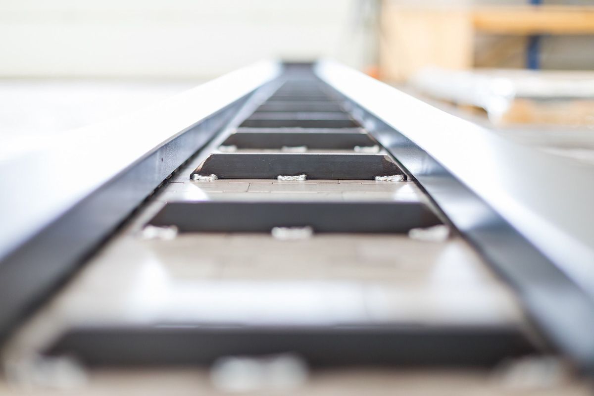 Förderband mit dunklen Metalllamellen und glänzenden Metallseiten, aus einem niedrigen Winkel betrachtet.