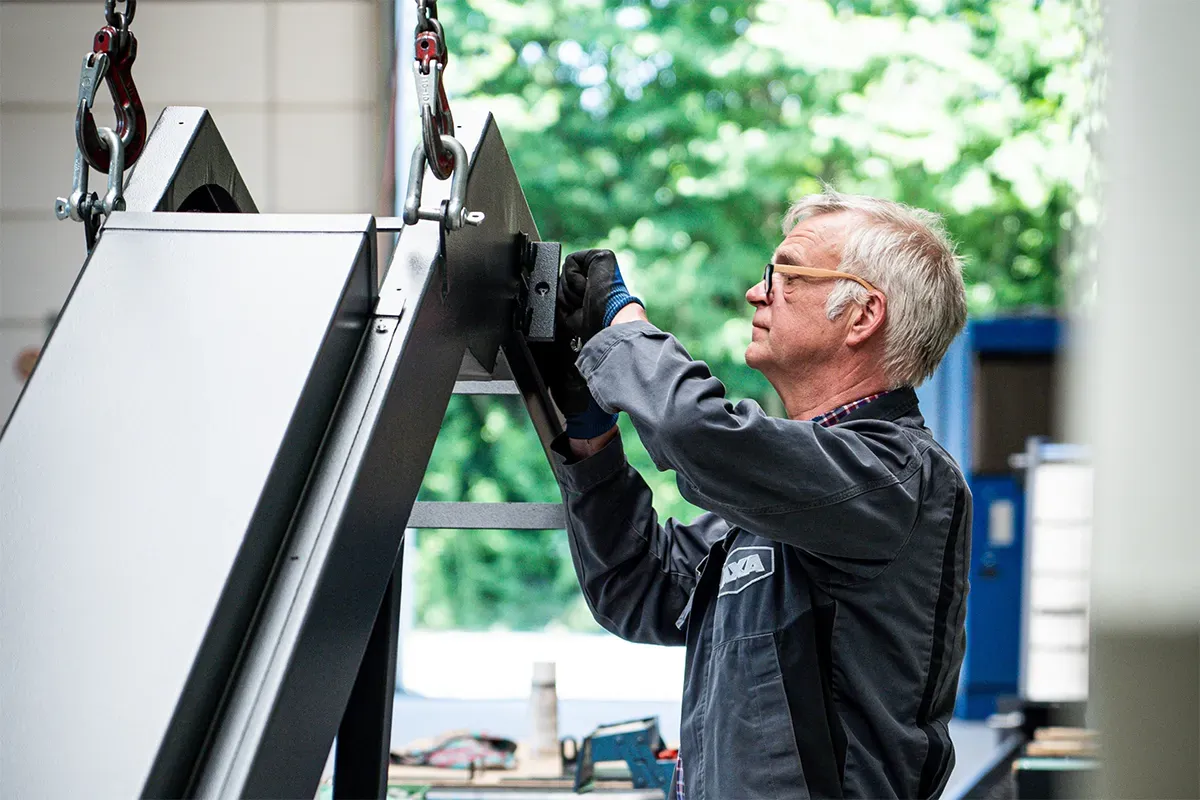 Mann in Arbeitskleidung montiert im Freien eine Metallkonstruktion.