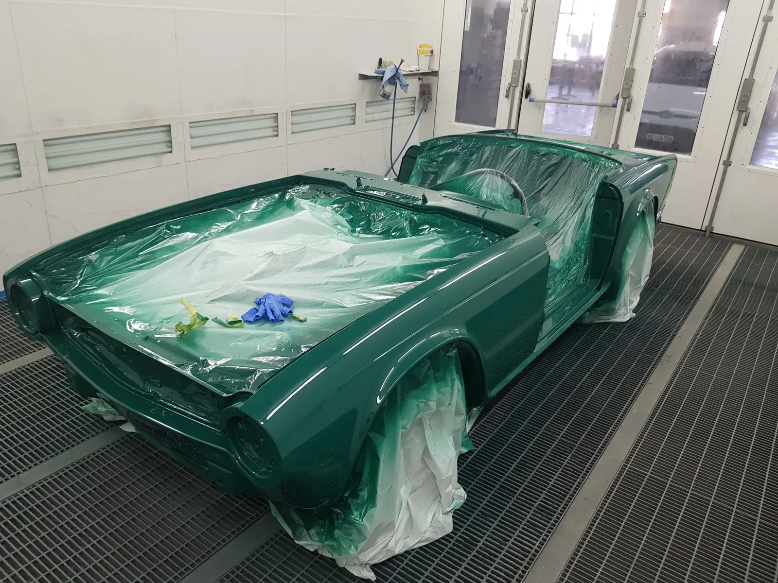 Voiture classique verte dans une cabine de peinture, recouverte de plastique pour la protéger.