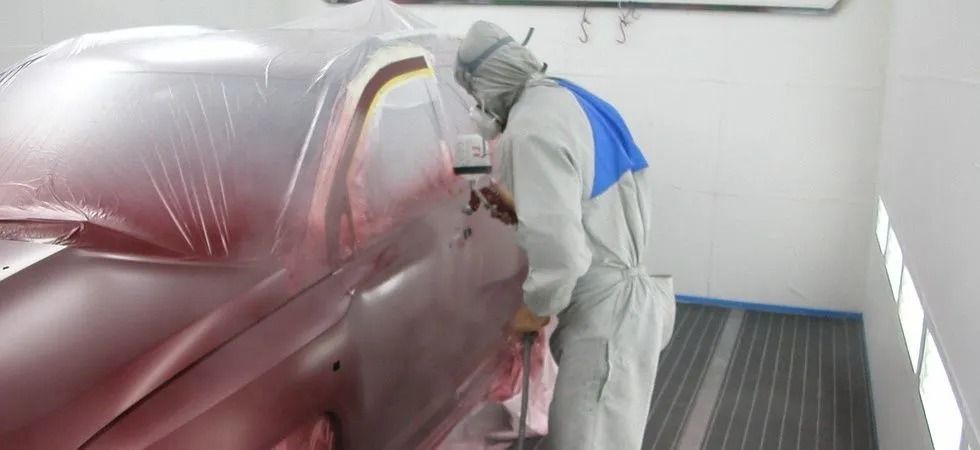 Dans un garage, une personne portant un équipement de protection pulvérise de la peinture sur la carrosserie d'une voiture