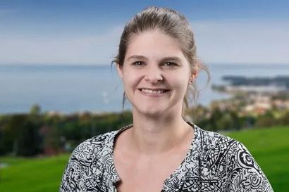 Lächelnde Frau in gemustertem Oberteil im Freien vor dem Hintergrund von Meer und Grünflächen