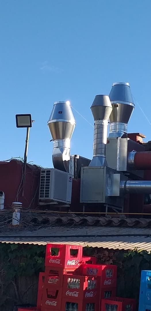 Tres conductos de ventilación metálicos en un tejado. Cielo azul brillante. Cajas de Coca-Cola en primer plano.