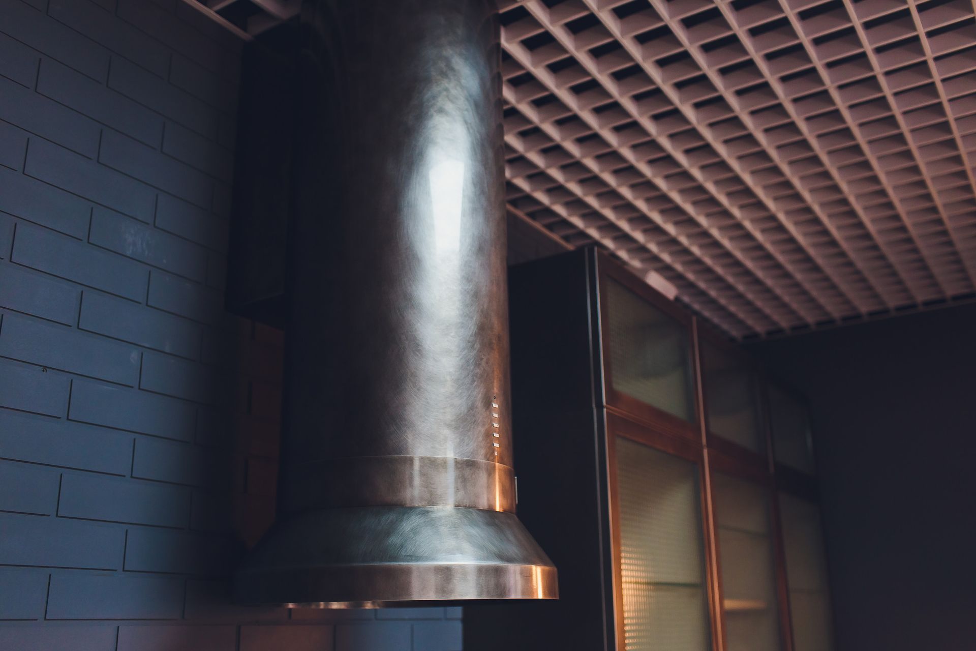 Una campana extractora de acero inoxidable cuelga del techo de una cocina.