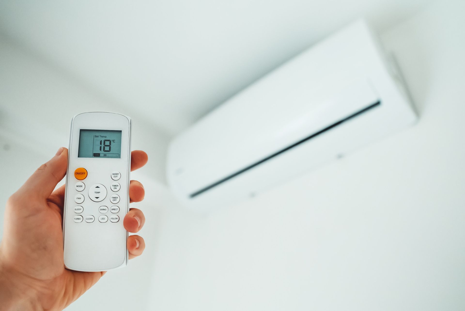 Una persona sostiene un control remoto frente a un acondicionador de aire.